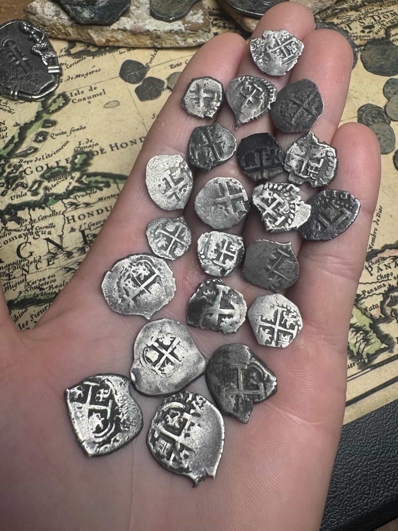 Full lot of Spanish colonial 1/2 and 1 reale silver cobs held in the hand over an antique map