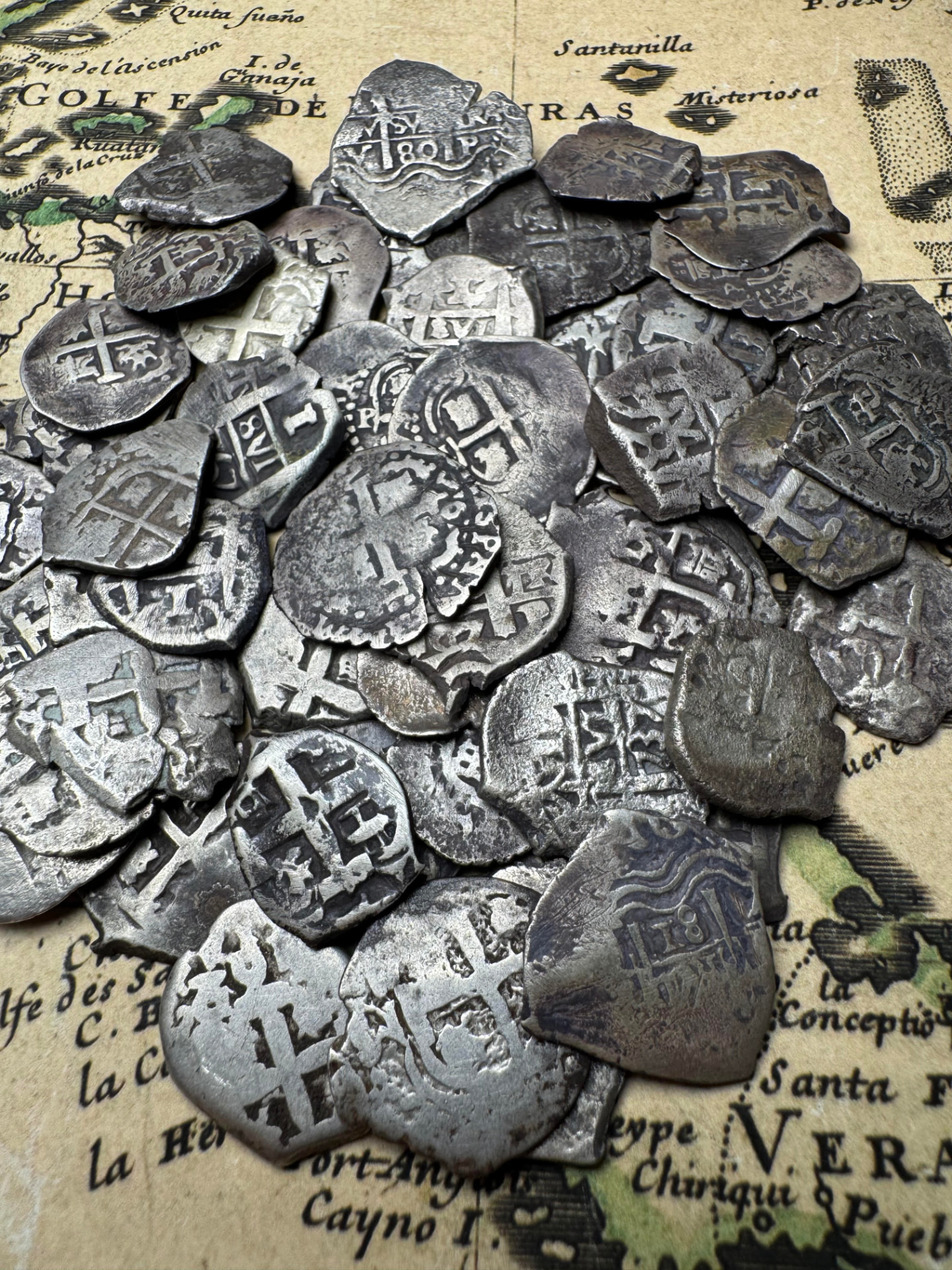 Large group of Spanish colonial 1 reale silver cobs on an antique chart